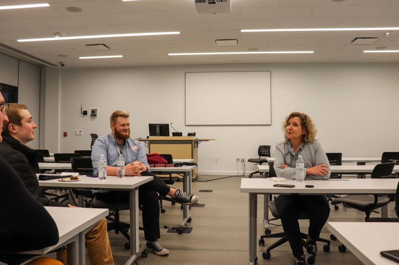 A man in a blue shirt looks on as a woman in a gray sweater talks during a meeting.