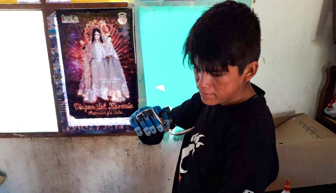 teen boy feeds grips a spoon with 3D printed prosthetic hand