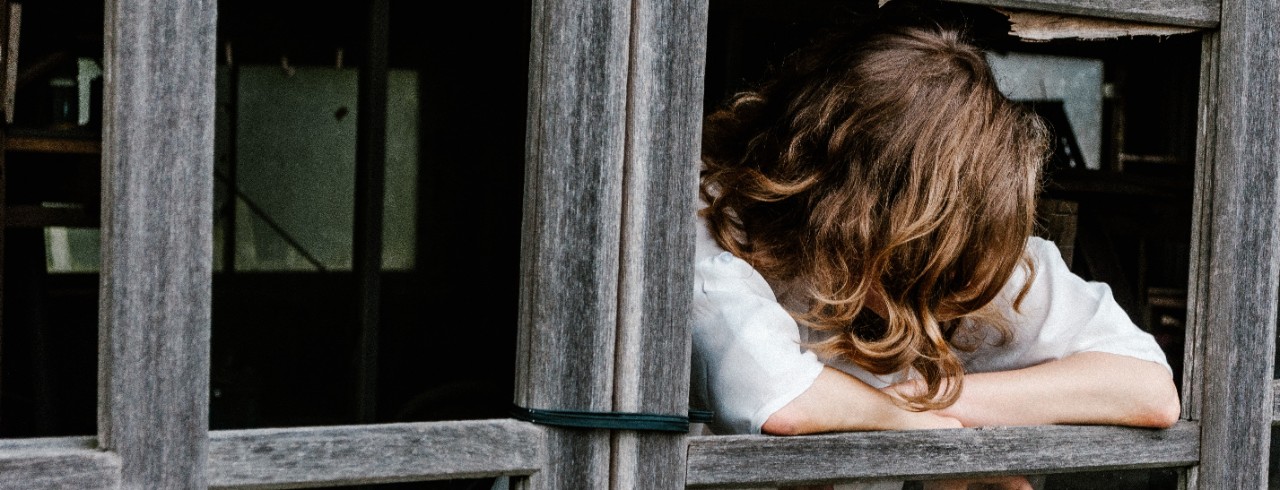 A woman leans against a window with her head down