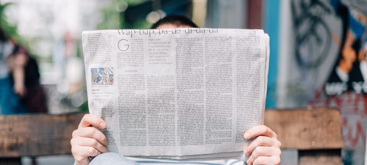 man reading a newspaper on a park bench