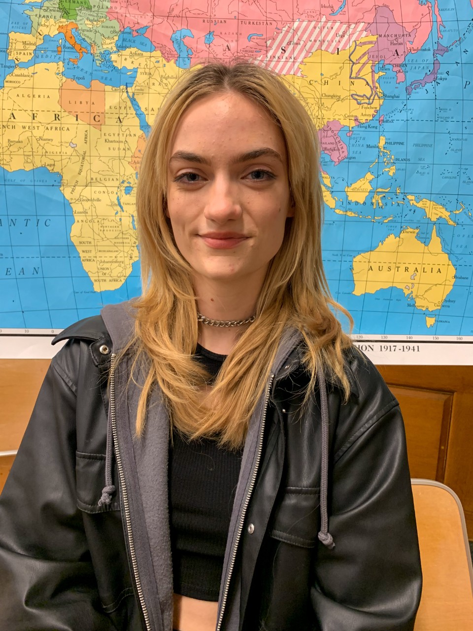 Lily Stiefel stands in front of a colorful world map in UC's McMicken Hall.