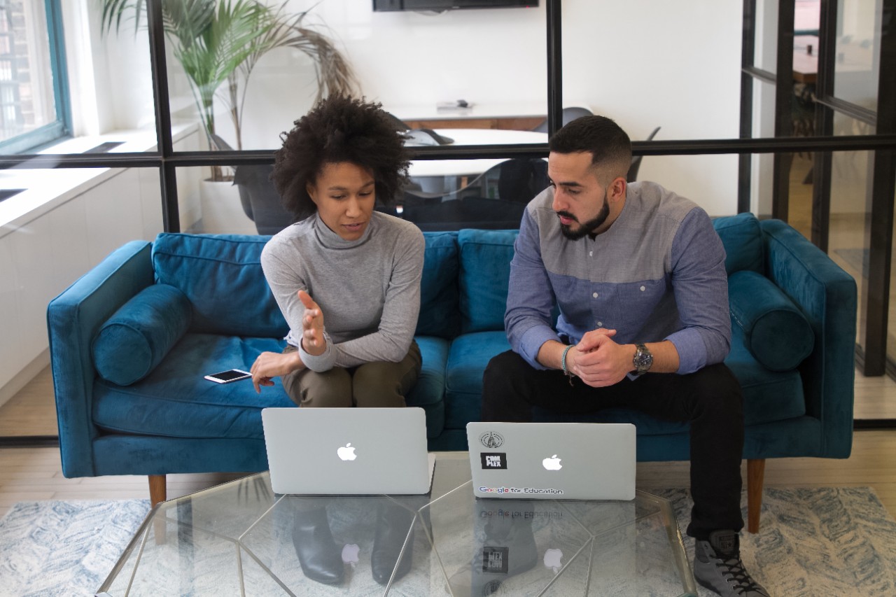 Two people sit on a couch in front of laptops.