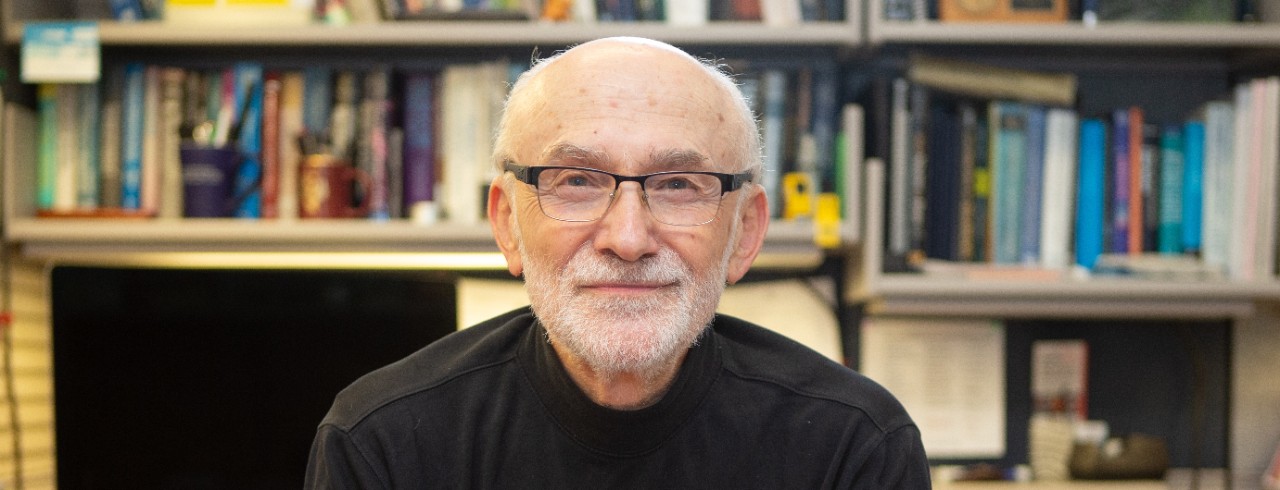 Professor Andrew Steckl sits at his desk in his office with shelves of books behind him