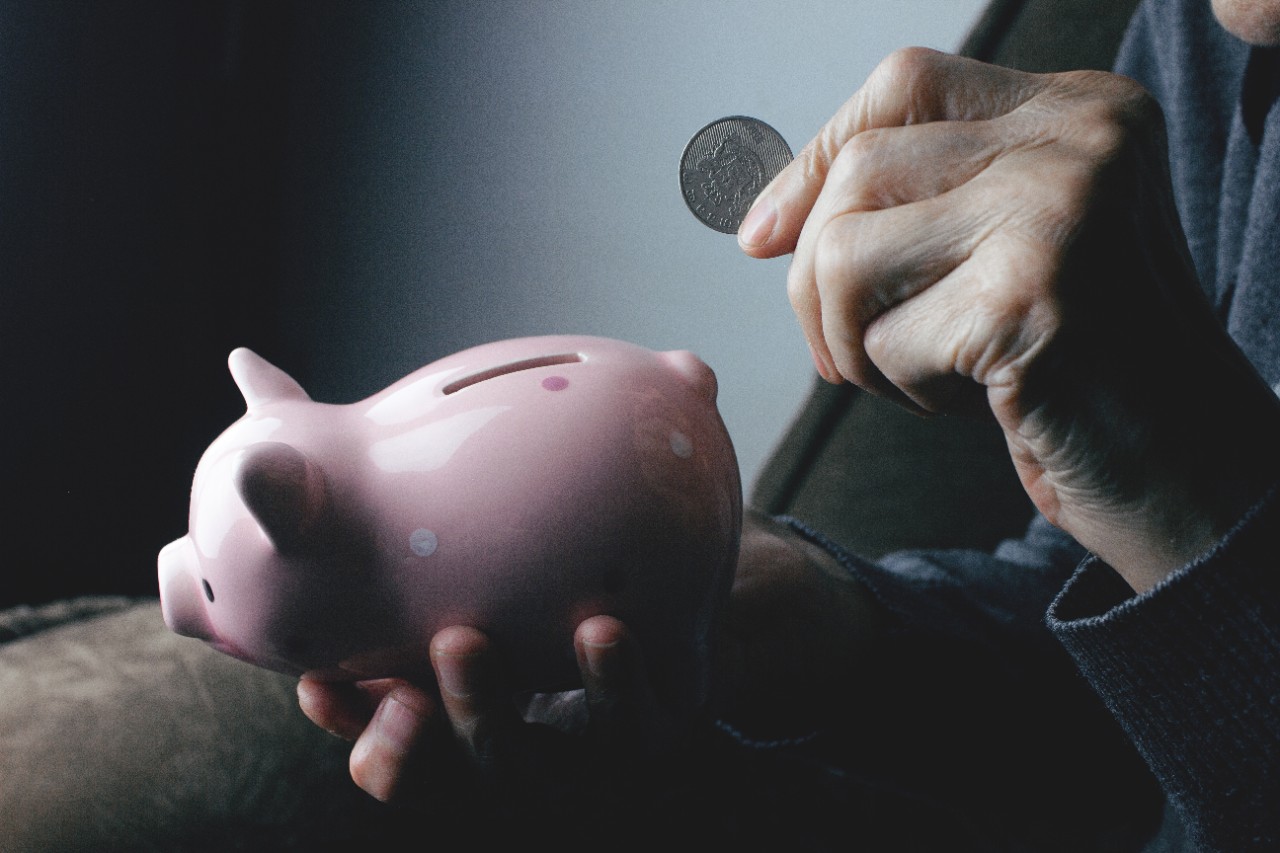 A hand puts a coin in a piggy bank.