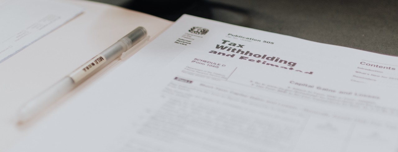 Tax forms in an open folder with a pen