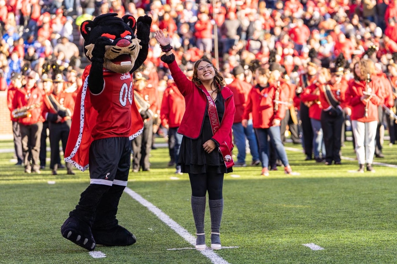 Yulia Martinez and the UC Bearcat mascot wave to the crowd on the field at Nippert Stadium.