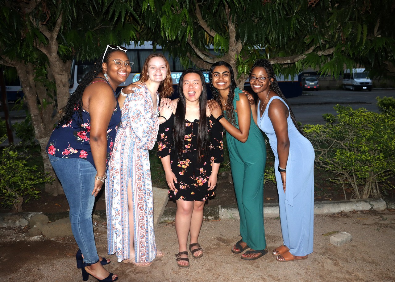 five young women pose in a row for the camera on a beach at night