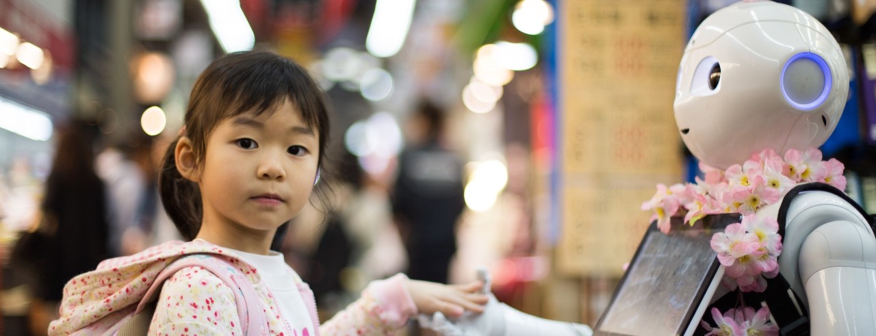Young girl shakes hand of a robot holding an iPad.