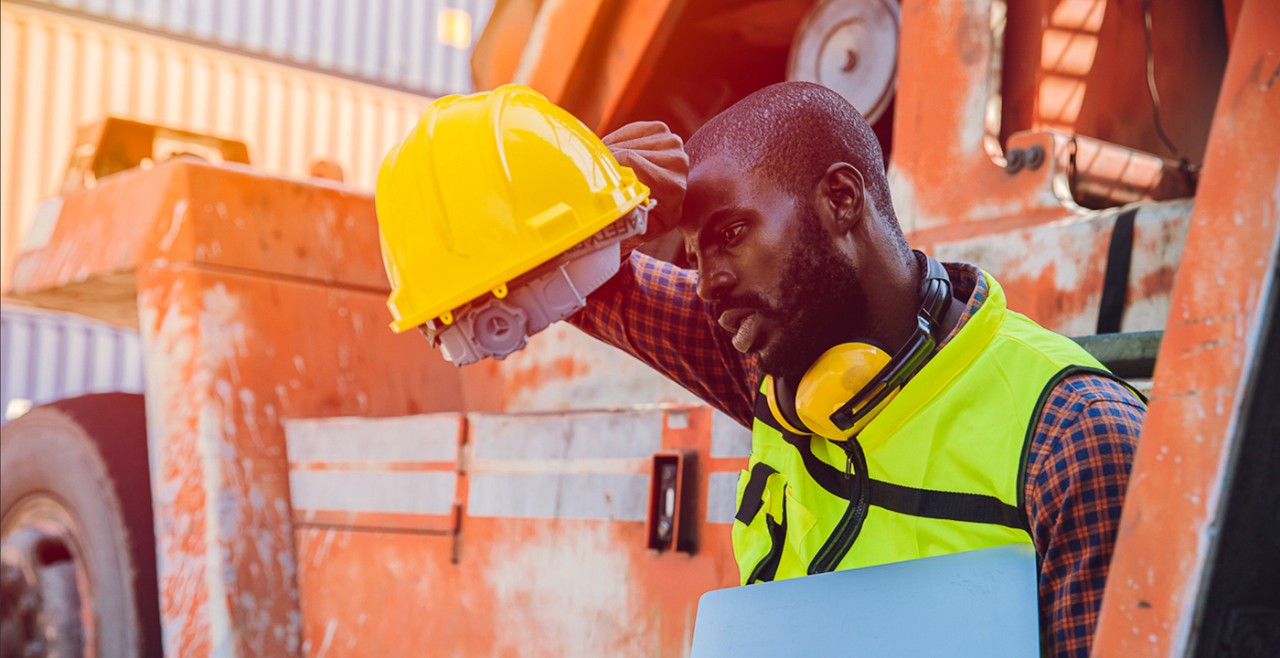 A construction worker holds a hardhat while mopping his brow.