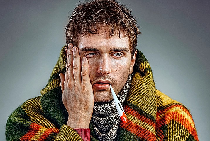 a photo of a man with a thermometer in his mouth battling a common cold