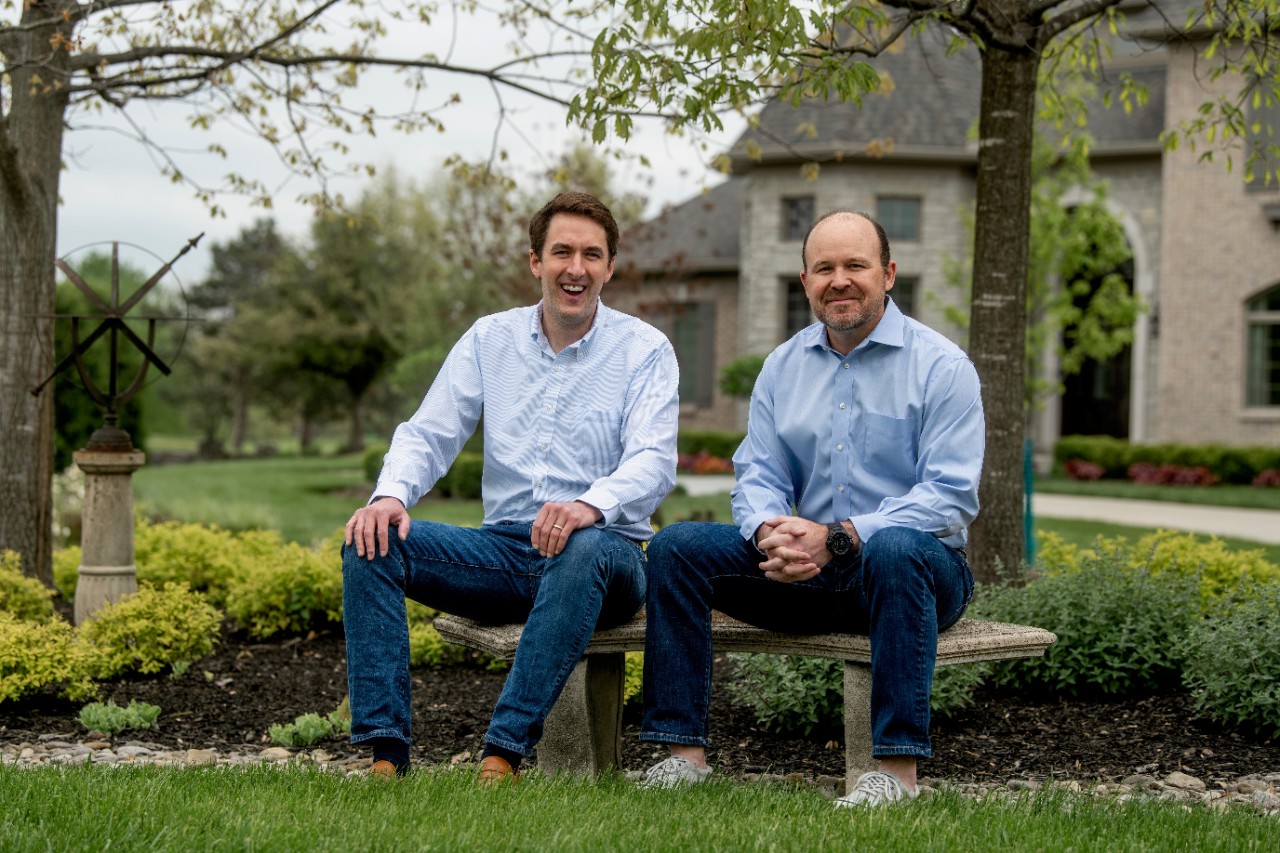 Two men sit in front of a house.