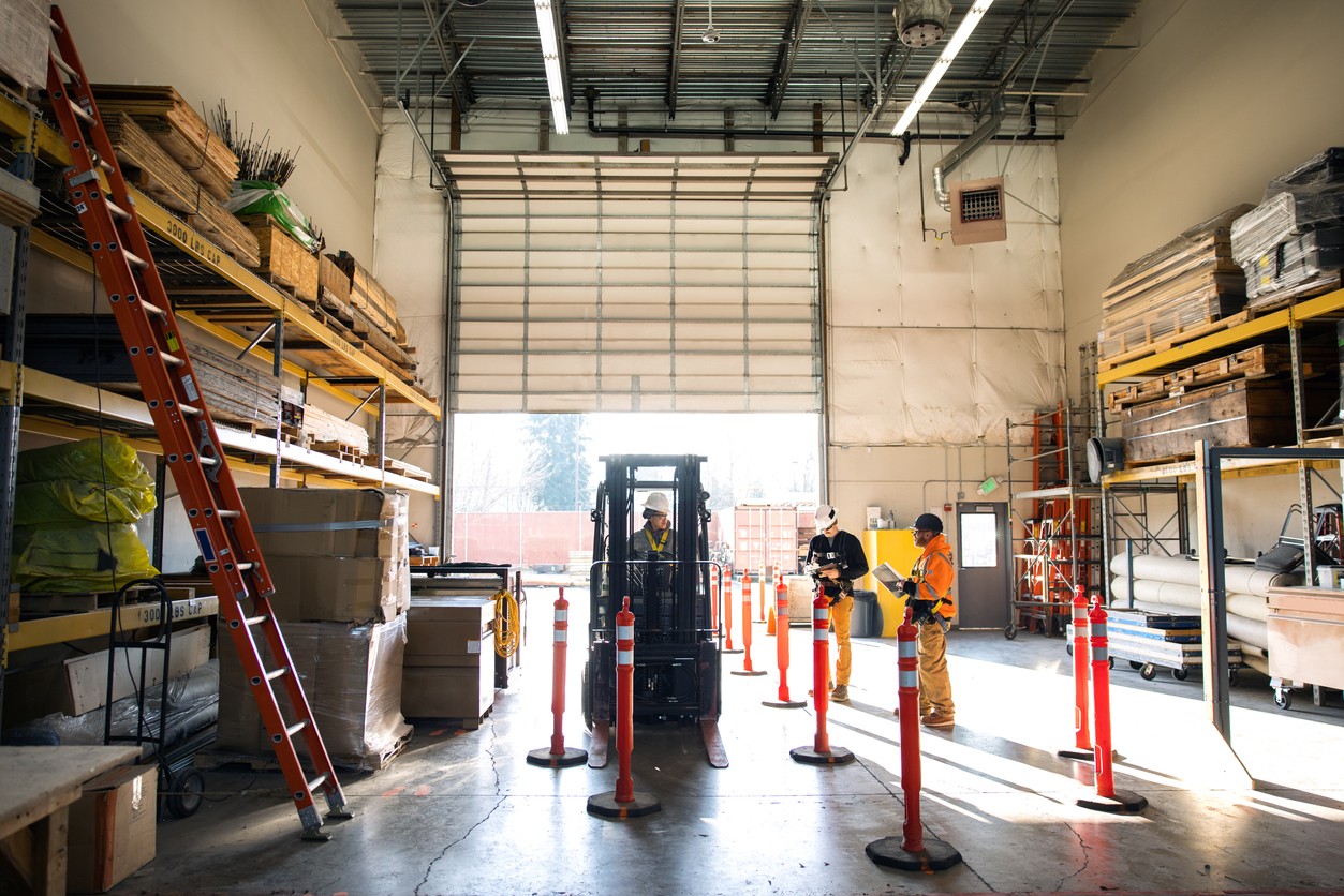 Woman riding a forklift, while other employees review paperwork