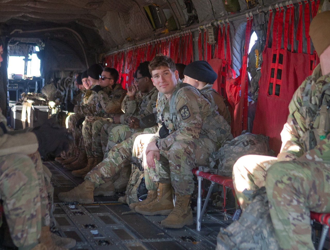 UC students in military fatigues lock their seatbelts in two rows of seats facing each other aboard a helicopter.
