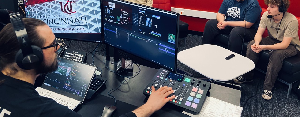 UC student Connor Bargeloh sits at a two-screen computer wearing a headset inside UC's Broadcast Studio.