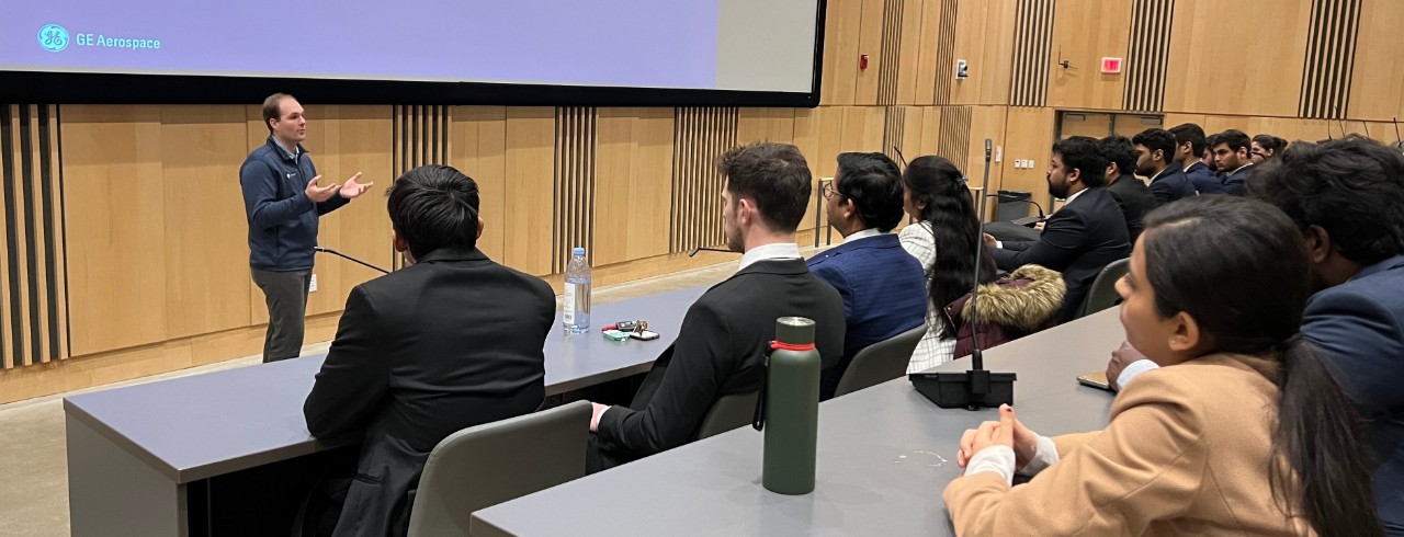 An instructor in professional dress addresses master's students.