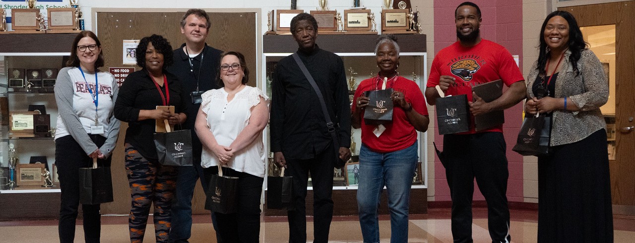 School staff members stand holding bags with UC logo