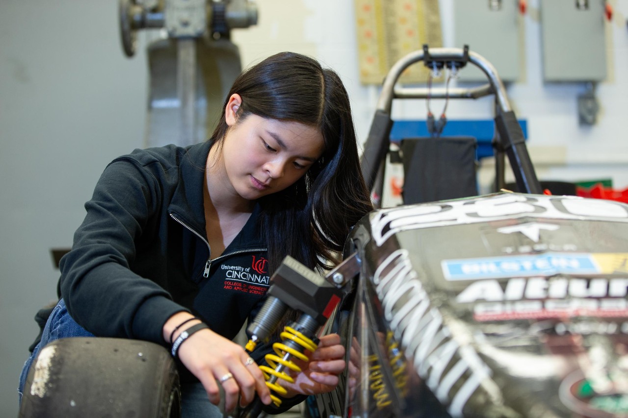 Emma Vail kneels over a Formula 1 car at Bearcat Motorsports.