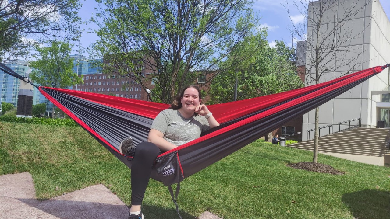 Woman sits in a red and black hammock and smiles at the camera.