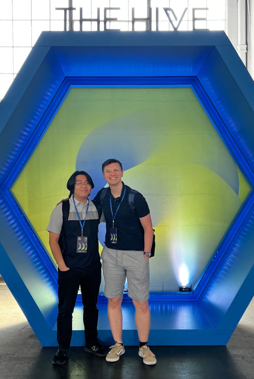 Two UC students tand in front of a large, honeycomb-shaped object.