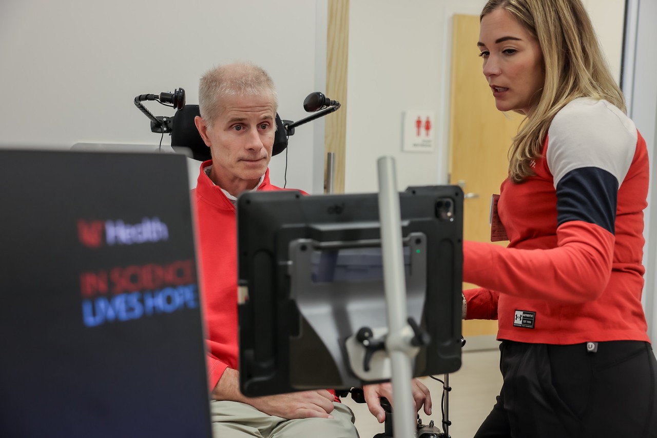Two people looking at screen. One person is standing. One is in a wheelchair. Both are wearing red.