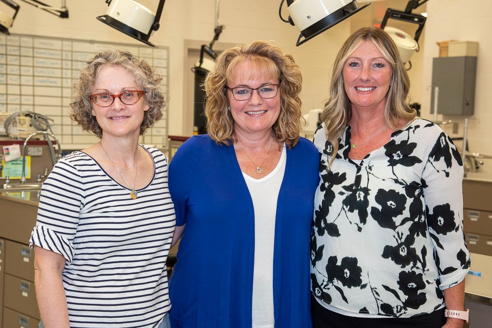 three professors standing together in an office and smiling