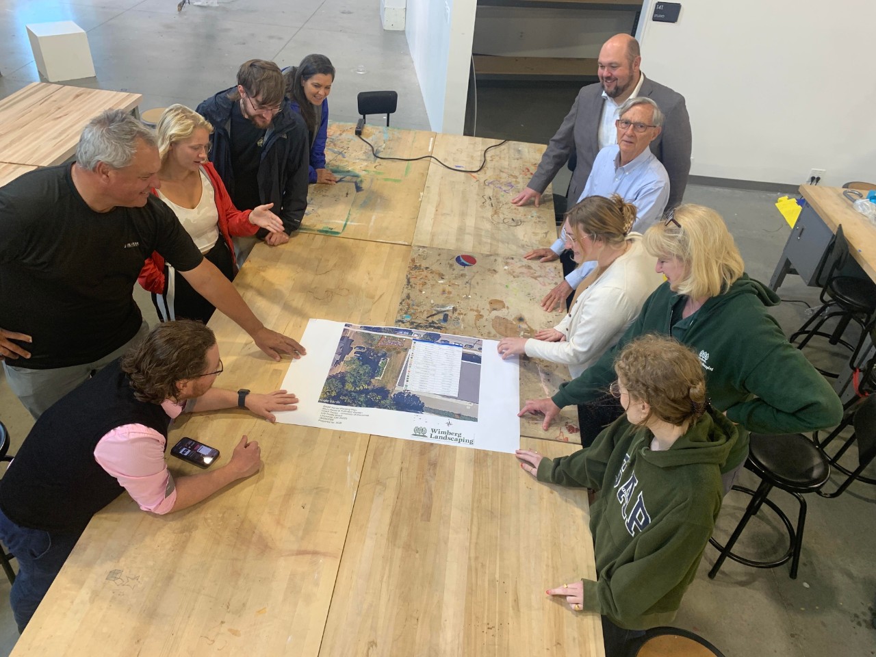 A group of people gather around a table to look at a diagram.