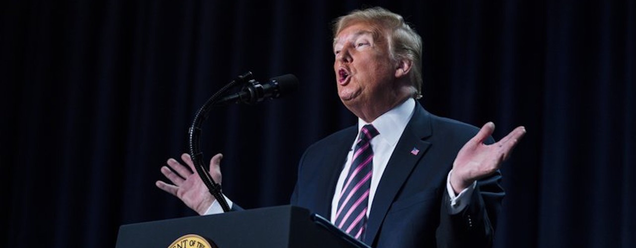 President Trump speaks and gestures from behind a podium.