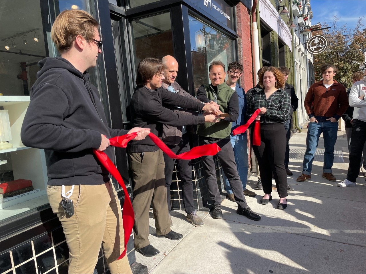 Stakeholders line up for a ribbon cutting outside of a store.