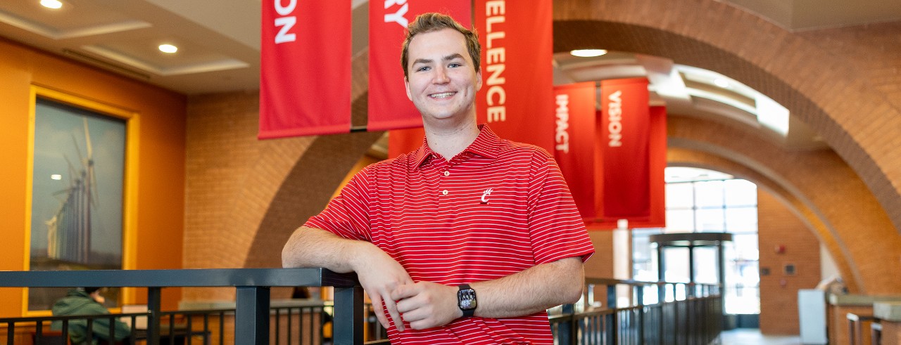 Alex Woodall is dress in UC swag and standing the UC College of Engineering building