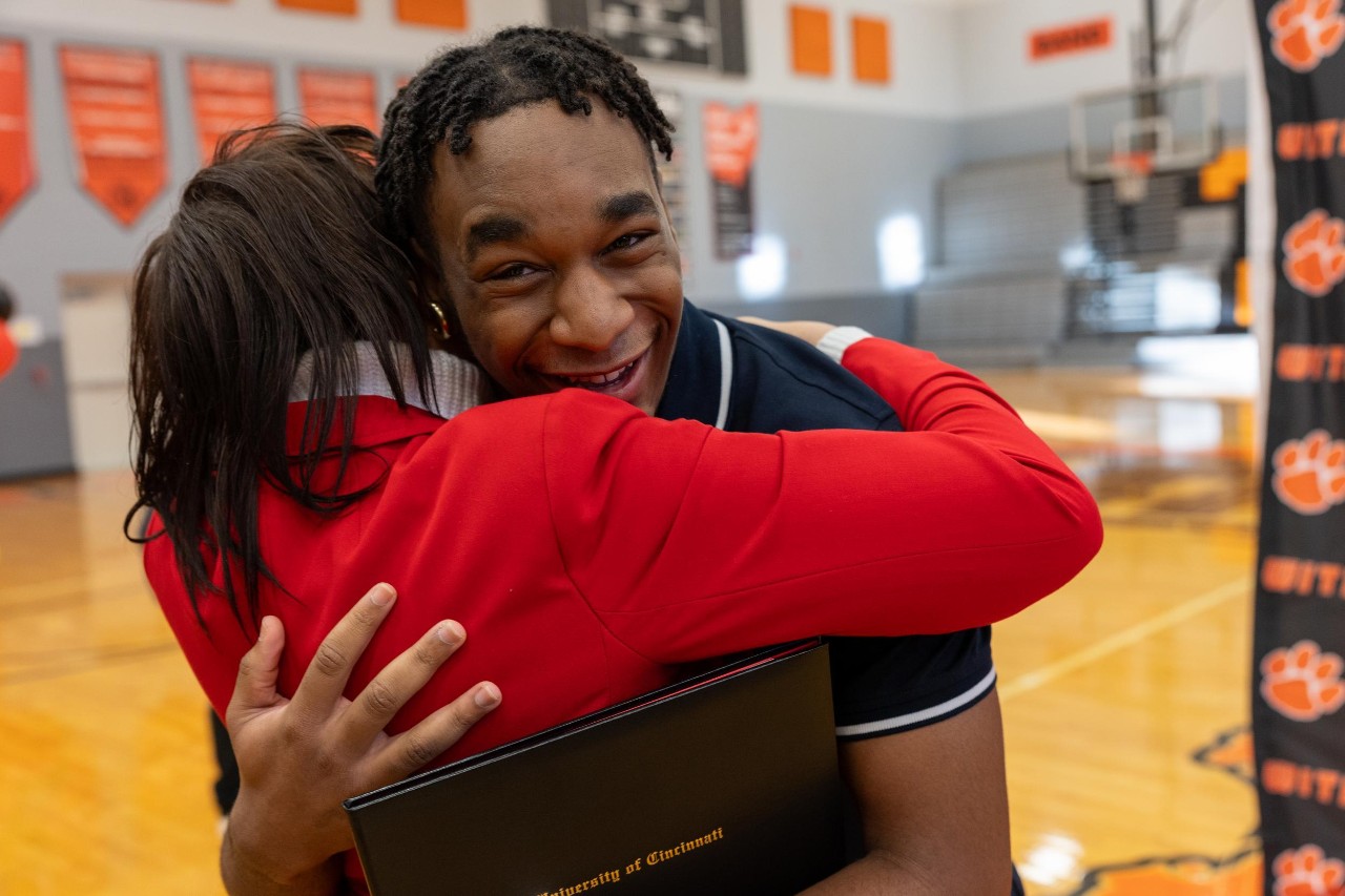 Oliver Tiani Vessah hugas a woman while holding his admission to UC