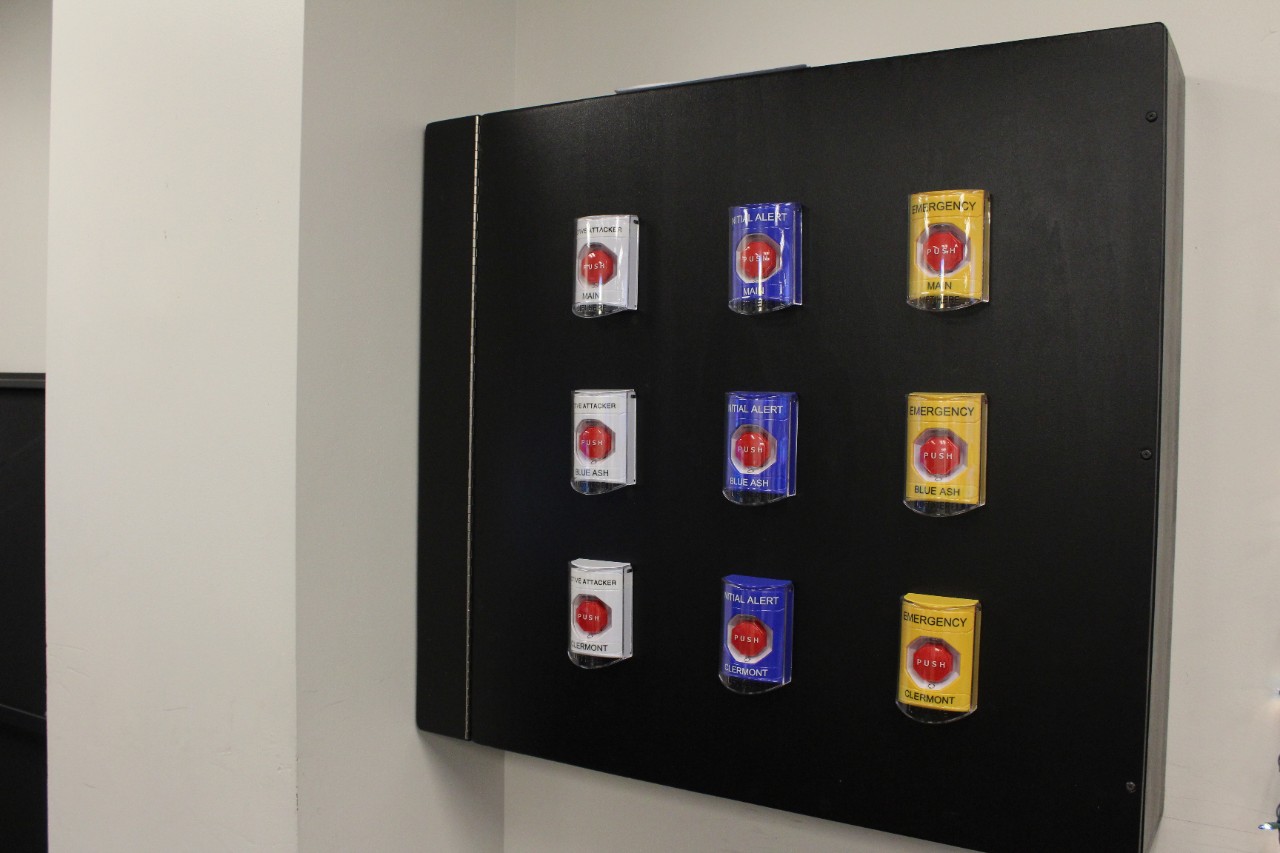 A black cabinet on the wall with three rows of three buttons that can be pressed in an emergency to quickly send an emergency alert.