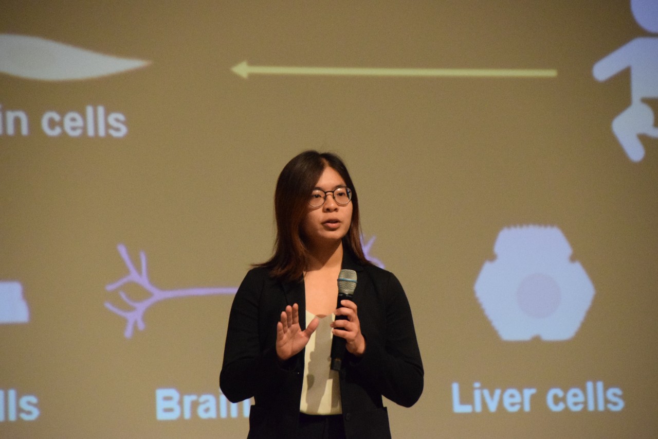 Nicole Pek uses a microphone in front of a PowerPoint screen.