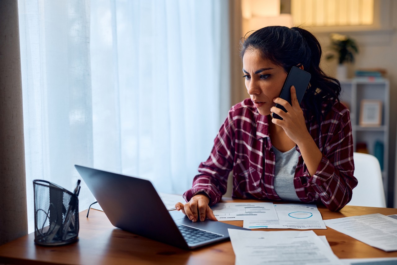 Woman shown sitting at a computer and answering a phone at home