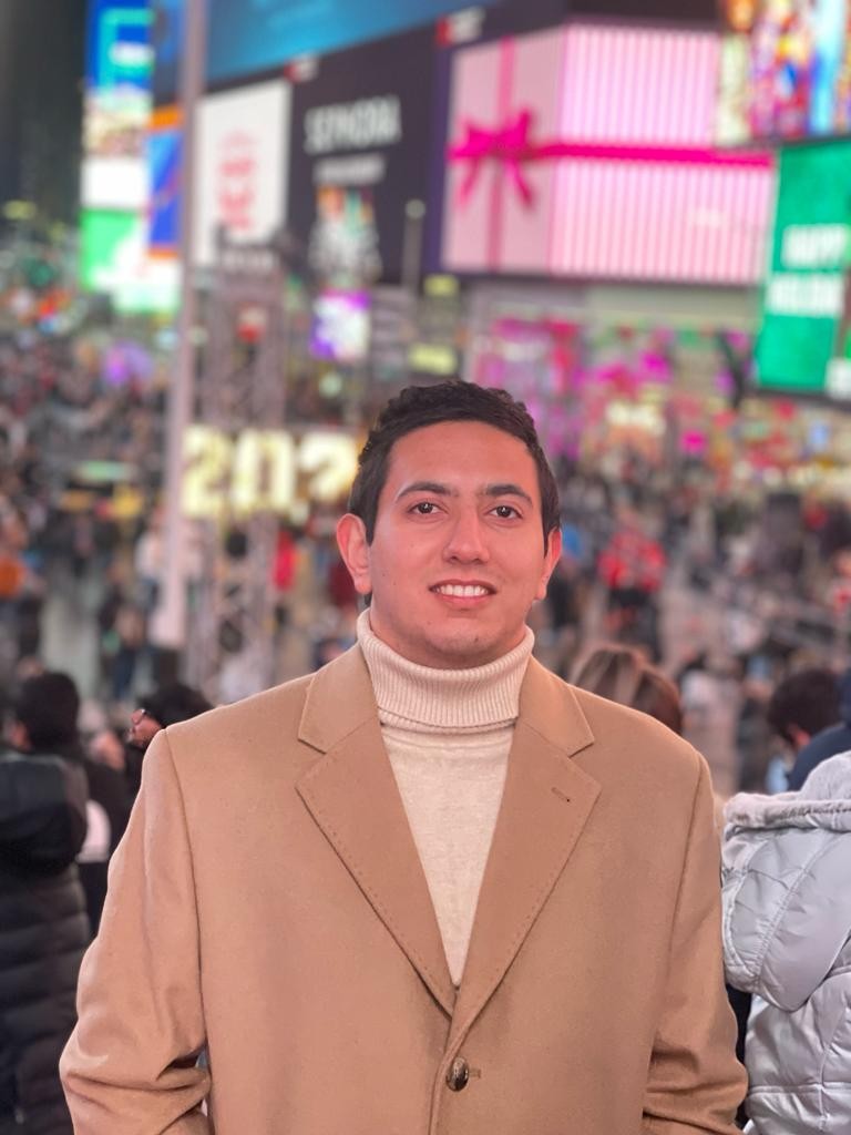 Manish Raj Aryal smiles at the camera. He is wearing a tan coat and white shirt. 