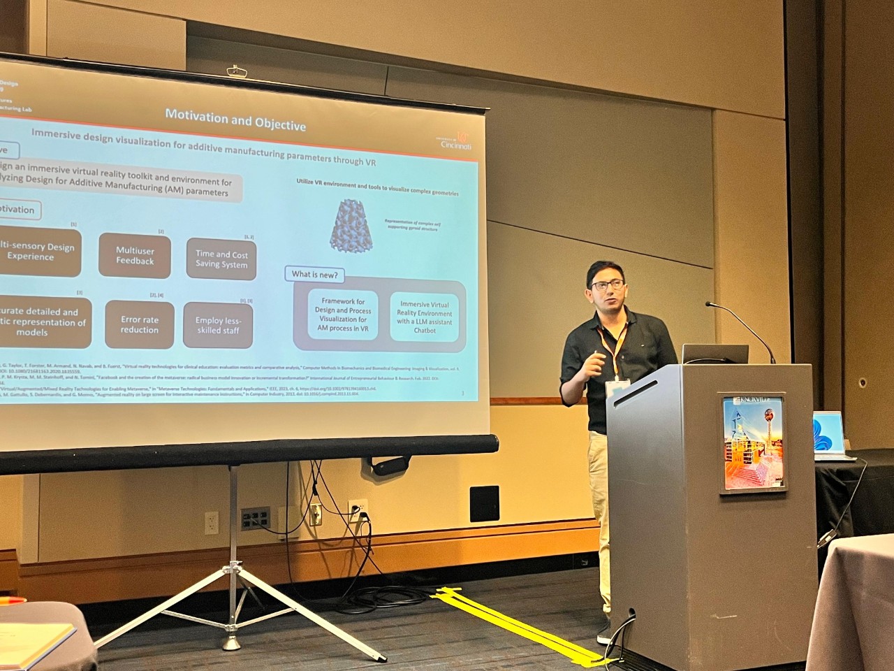 Manish Raj Aryal stands at a podium and gives a presentation. A large board with information is behind him. 