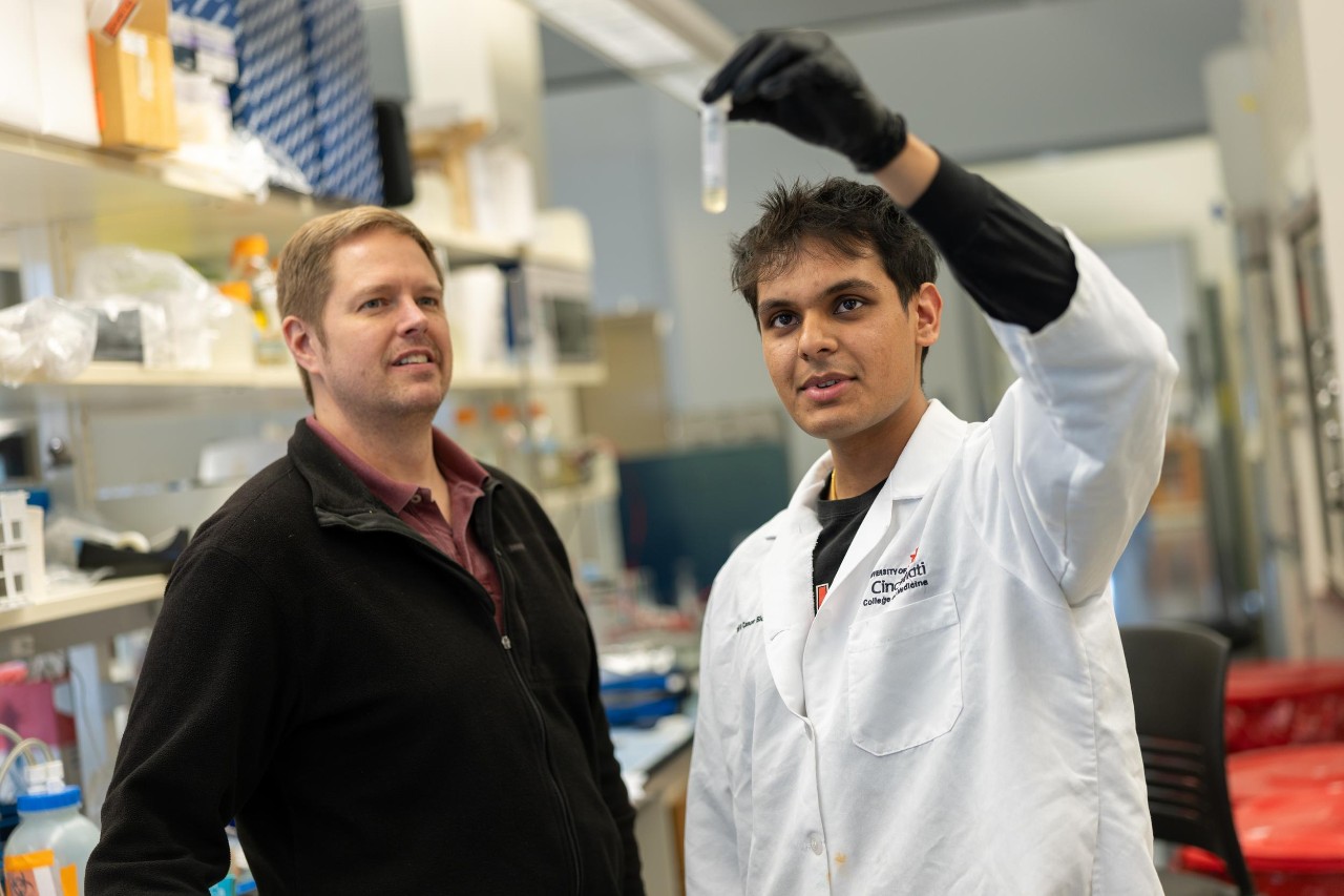 Jay Patel holds up a vial in a lab while Tom Cunningham looks on