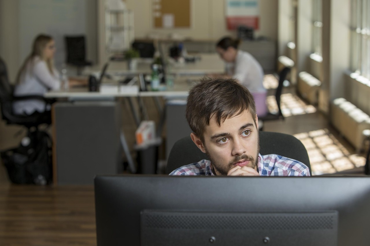 Male student sits in front of a computer looking off into the distance