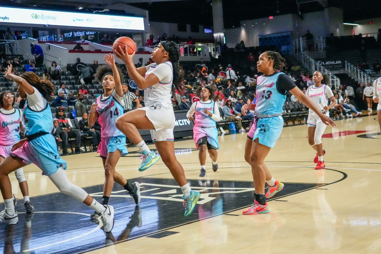 half a dozen high school girls are on the basketball court and one takes a shot with a basketball