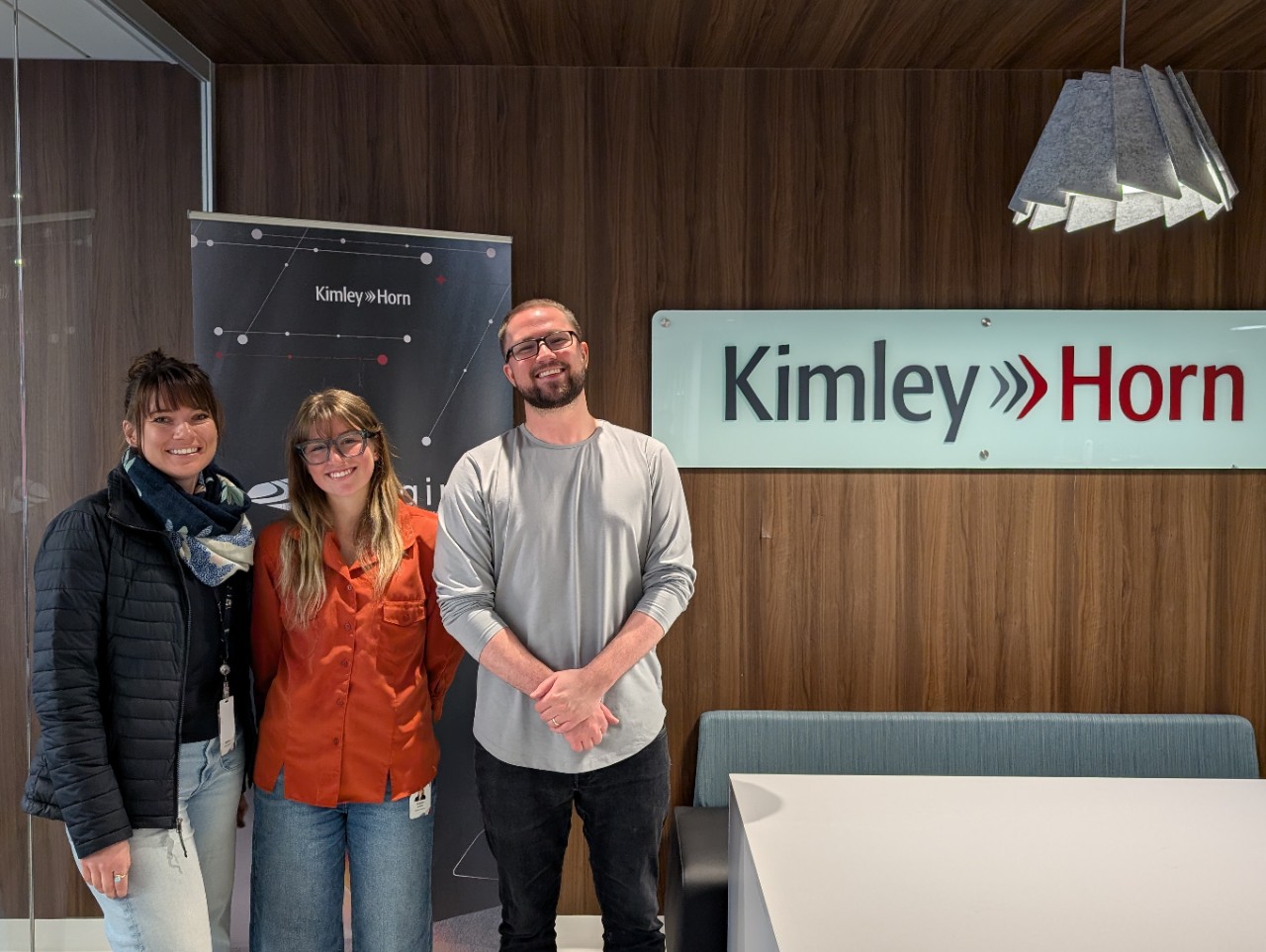 Sophia Gartland flanked by her supervisors at Kimley-Horn, standing in front of a Kimley-Horn banner 