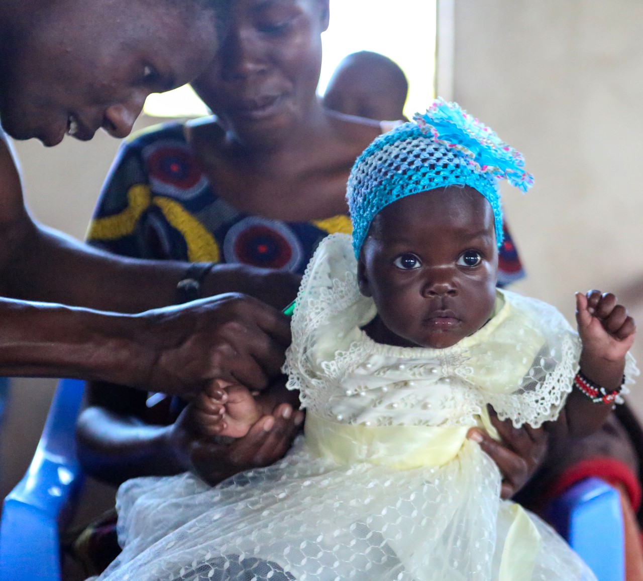 A Tanzanian medical staff applies a bandaid to a baby girl sitting on her mother's lap.