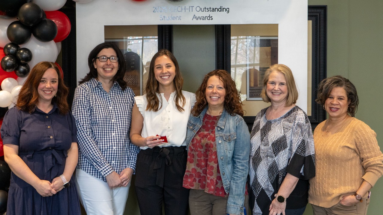 student stands with outstanding student award surrounded by faculty members, all smiling