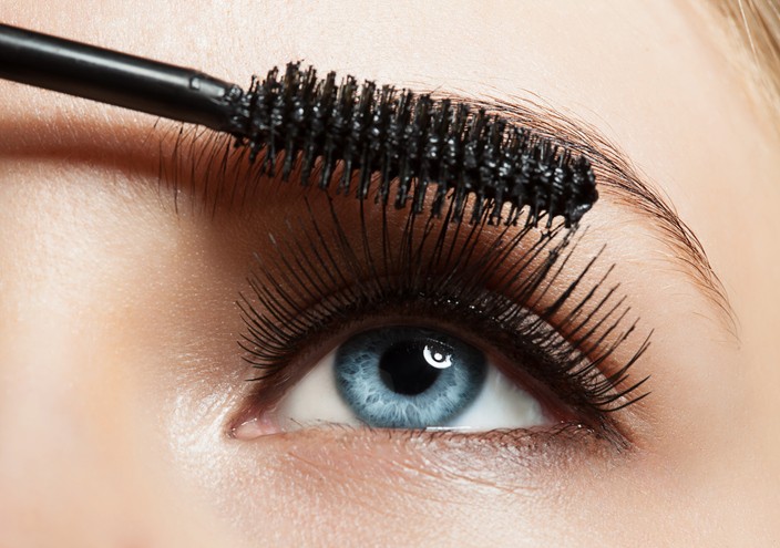 A person applying black mascara to eyebrows