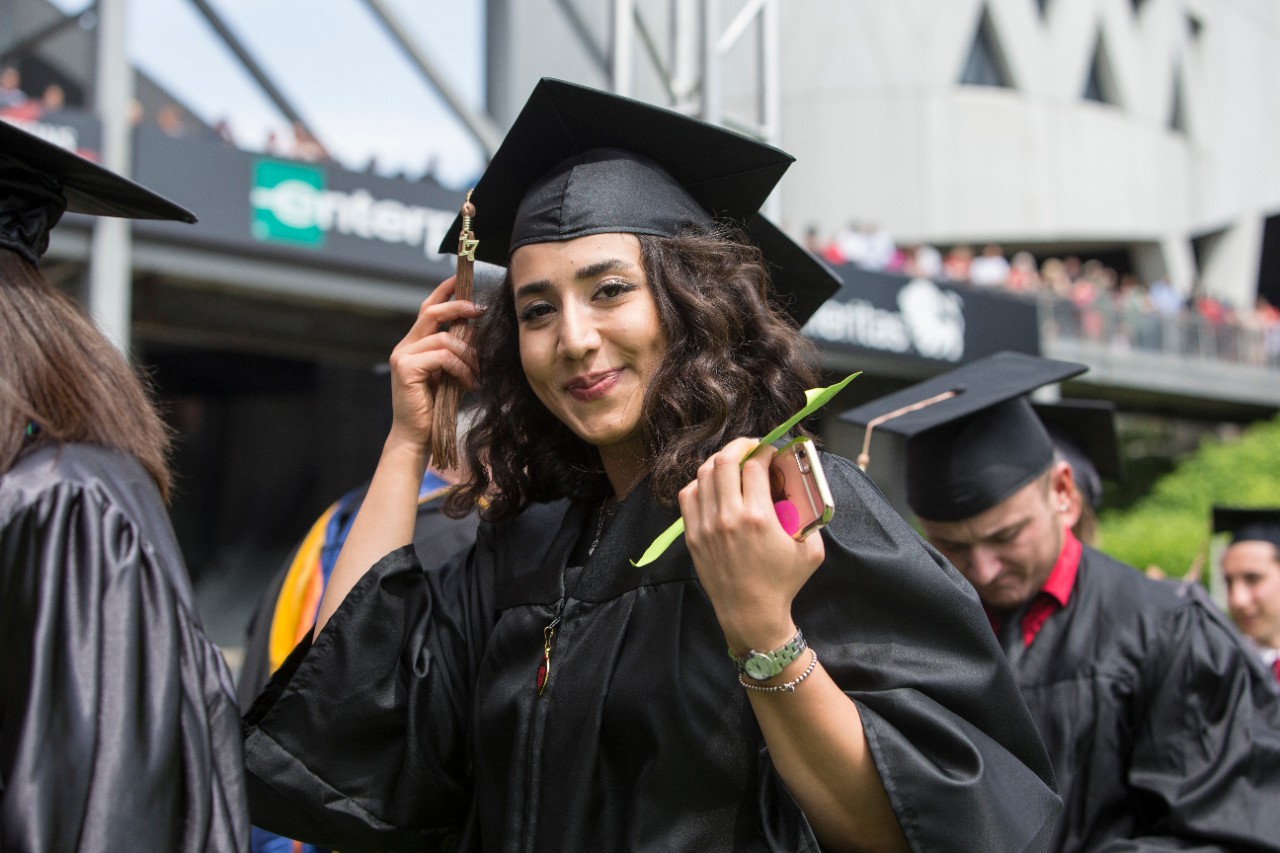 A UC student at Graduation in a cap and gown smiling at the camera
