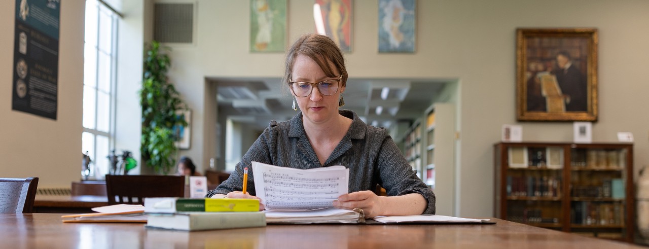 Anna Conser sits at a table in a library reading sheet music.