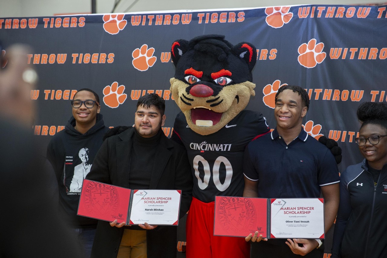 Two Marian Spencer Scholarship winners stand with the UC Bearcat Mascot and hold scholarship ceritificates