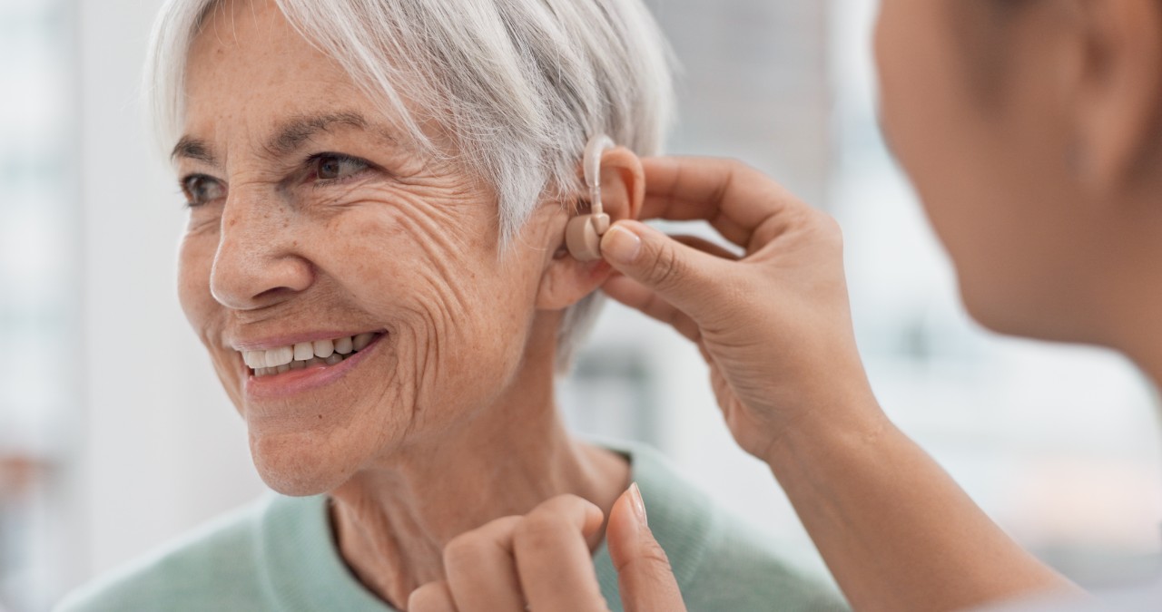 A health care provider places a hearing aid on a woman's ear