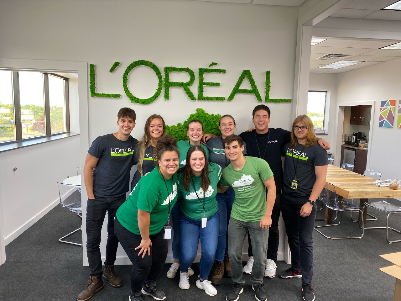 Group of L'Oreal co-ops pose in front of a green L'Oreal sign