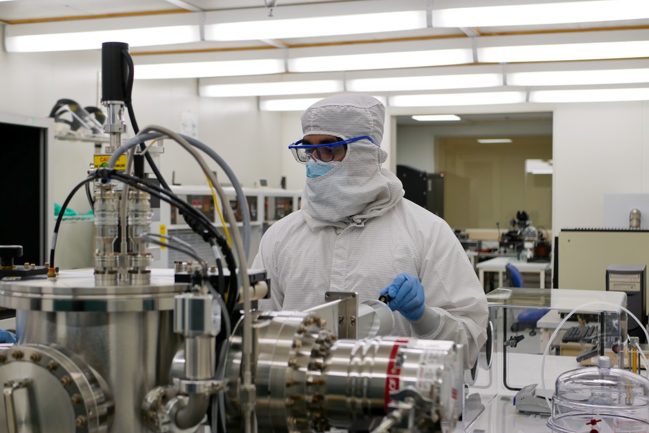 A student in protective clothing works at a machine in a cleanroom.