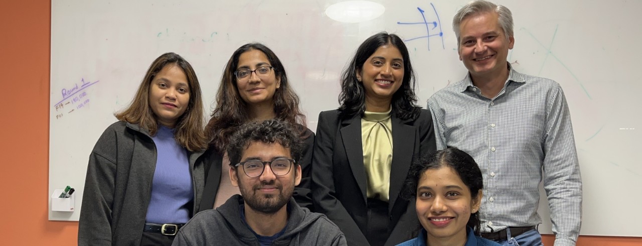 Five students and Lindner adjunct professor Kyle Snyder (back right) pose in front of a white board in a Lindner Hall conference room.