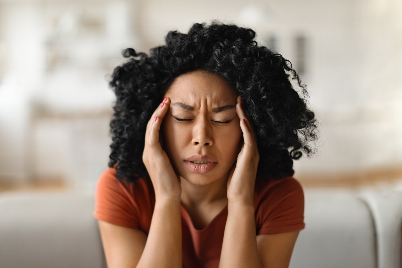 A woman holds her hands to the sides of her face as she suffers from a migraine